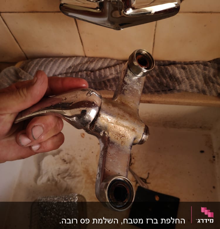 ברז מתכת מפורק מוחזק ביד מעל כיור